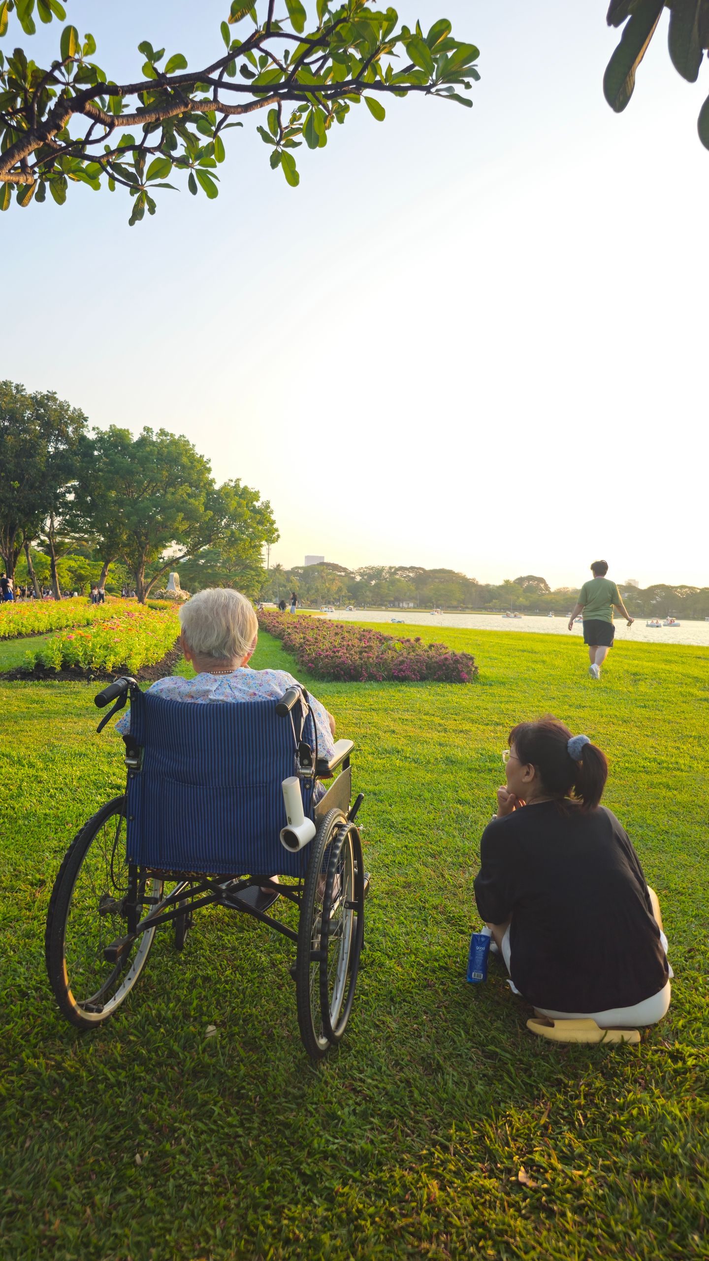 Elderly person and caregiver enjoy a serene afternoon by the river in Bangkok.